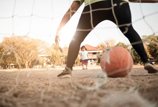 Cute little Asian child playing football with her mother on playground on summer day. Happy family spending free time together.