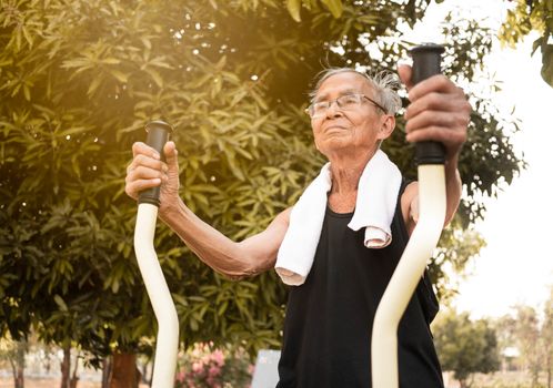 Asian senior man in sporty clothes exercising for good health on outdoor fitness equipment in a public park on sunshine day. healthy lifestyles concept.