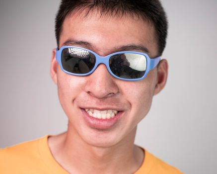 Close up portrait of a young handsome teenager boy in yellow long sleeve t-shirt and wear black glasses, smiled on grey background. lifestyle people concept.