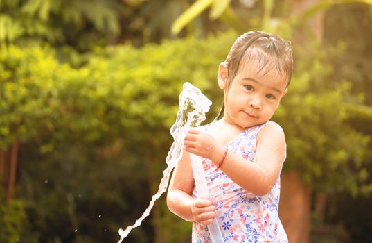 Cute little girl playing a rubber hose spraying water with sunlight in the backyard. Children enjoy outdoor activities on hot summer days.