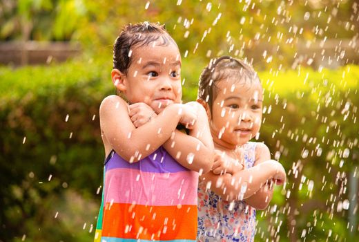 Cute little girl having fun in rainy at backyard. Children enjoy outdoor activities on hot summer days.