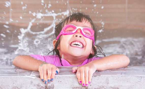 Cute little girl in swim glasses having fun in swimming pool. Children enjoy outdoor activities on hot summer days.