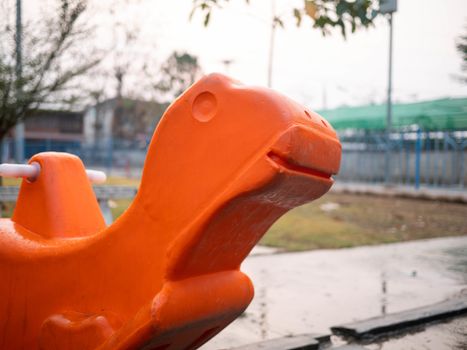 Orange plastic rocking horse in playground outdoors.