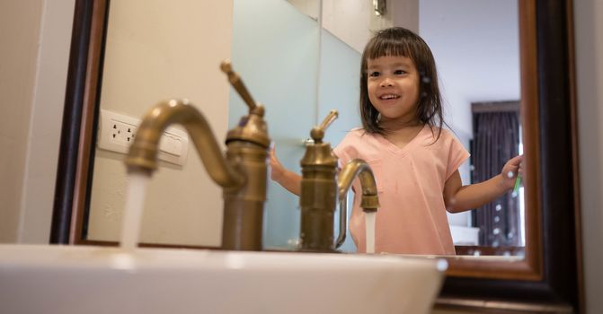 Happy Asian little child girl brushing teeth in the bathroom in morning. Oral hygiene concept.