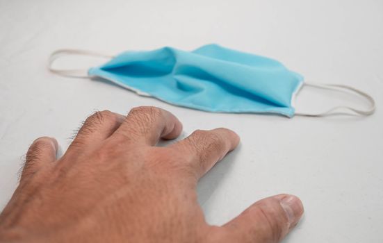 Human reaching out your hand to pick a homemade cloth face mask that placed on table, use for protection from air pollution or virus epidemic. Scarce medical mask concept.