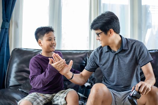 Asian father and son enjoy playing video games together with video joystick with excite and very fun in the living room at home