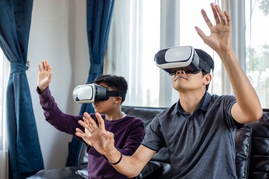 Asian father and son enjoy playing video games together with video joystick and Virtual Reality Glasses with exciting and very fun in the living room at home