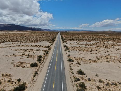 Aerial view of endless desert straight dusty asphalt road in Joshua Tree Park. USA. Long straight tarmac road heading into the desert to the direction of Arizona.