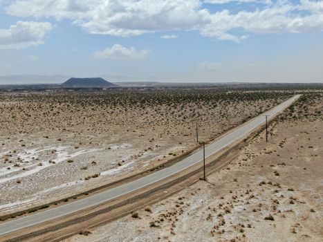 Aerial view of endless desert straight dusty asphalt road in Joshua Tree Park. USA. Long straight tarmac road heading into the desert to the direction of Arizona.