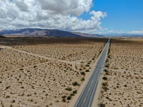Aerial view of endless desert straight dusty asphalt road in Joshua Tree Park. USA. Long straight tarmac road heading into the desert to the direction of Arizona.