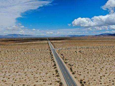 Aerial view of endless desert straight dusty asphalt road in Joshua Tree Park. USA. Long straight tarmac road heading into the desert to the direction of Arizona.