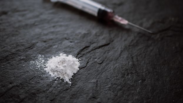 drug addict concept. close up of drug syringe and cooked heroin on black background