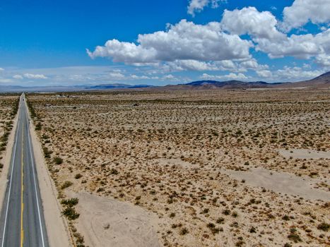 Aerial view of endless desert straight dusty asphalt road in Joshua Tree Park. USA. Long straight tarmac road heading into the desert to the direction of Arizona.