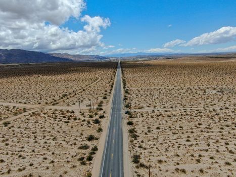 Aerial view of endless desert straight dusty asphalt road in Joshua Tree Park. USA. Long straight tarmac road heading into the desert to the direction of Arizona.