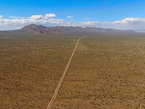 Aerial view of endless desert straight dusty asphalt road in Joshua Tree Park. USA. Long straight tarmac road heading into the desert to the direction of Arizona.