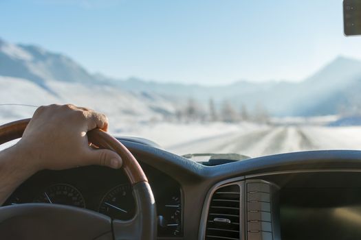 Close-up of a man's hand on the steering wheel of a car that moves on a snowy road among the mountains in the winter
