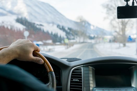 Close-up of a man's hand on the steering wheel of a car that moves on a snowy road among the mountains in the winter