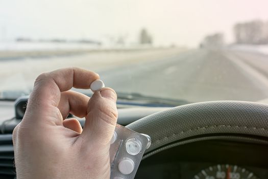 driver hand holding a bag of pills while driving on the highway