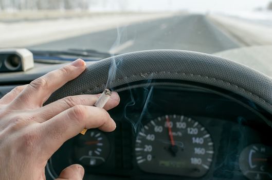 a Smoking cigarette in the hand of a Smoking car driver while driving on a snowy highway against the background of the speedometer on the dashboard