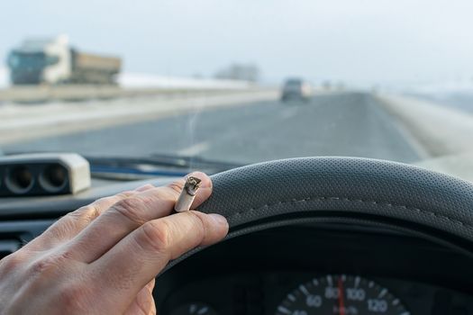 a Smoking cigarette in the hand of a Smoking car driver while driving on a snowy highway against the background of the speedometer on the dashboard