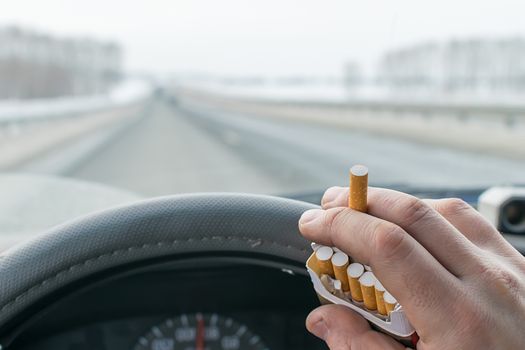 View of a car driver hand holding a pack of cigarettes while driving on the highway