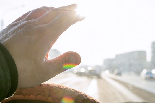 The hand of the driver of the car covers the sunlight, which blinds the person to see the road situation