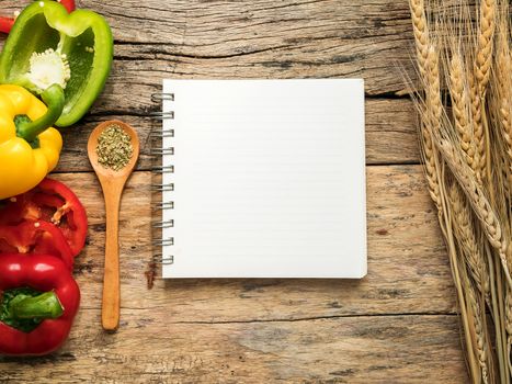 flat lay of blank recipe cooking book and utensils with herbs and colorful bell pepper over wooden background. top view with copy space. food recipe and cooking concept