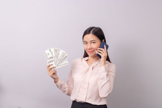 Asian beautiful woman holding banknote money in hand and mobile phone in another hand isolated on grey background. commercial business by phone concept