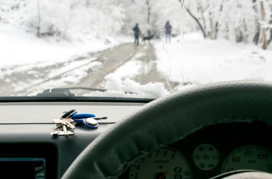 a bunch of keys lies on the dashboard of the car on the background of walking people on a wet snow-covered road outside the window in the winter