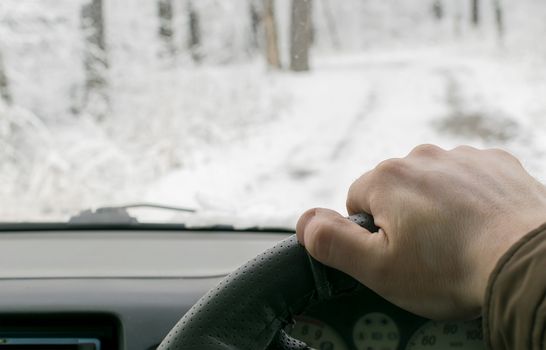 Man's hand on the steering wheel of a car that moves in the snowy forest on a wet slushy road