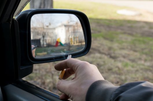 close-up, smoking cigarette in the hand of a man, the driver, in the car, which is in the Parking lot