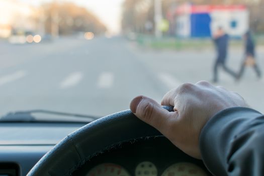 view from the car, the man's hand on the steering wheel of the car, located opposite the pedestrian crossing and pedestrians crossing the road