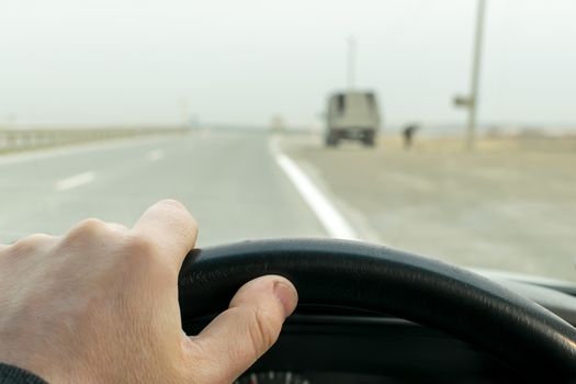 View of driver's hands on the wheel of a car that travels on the highway near parked on the side of the truck