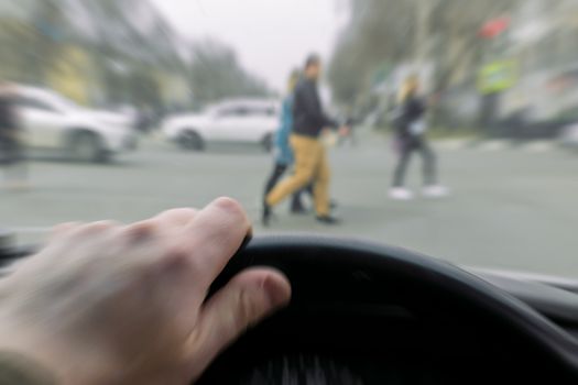 Emergency. View from the car, a man's hand on the steering wheel of the car while braking, in front of a pedestrian crossing and pedestrians crossing the road