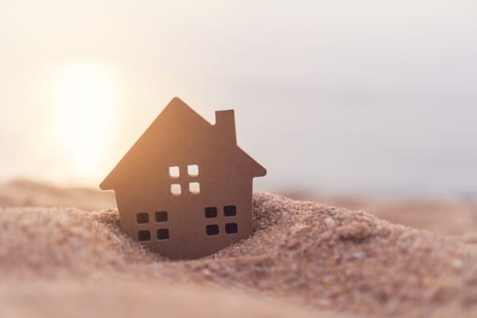 Model of a little house on sand with nature beach background. Dream life concept.