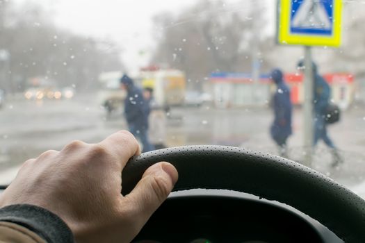 view from the car, the man's hand on the steering wheel of the car, located opposite the pedestrian crossing and pedestrians crossing the road