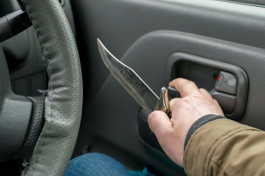 View of the knife in the hand of the driver inside the car, which is going to open the door