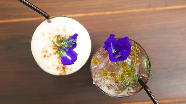 two glasses of drink, coffee and italian soda menu on the table at coffee shop decorate with pea flower and green grass