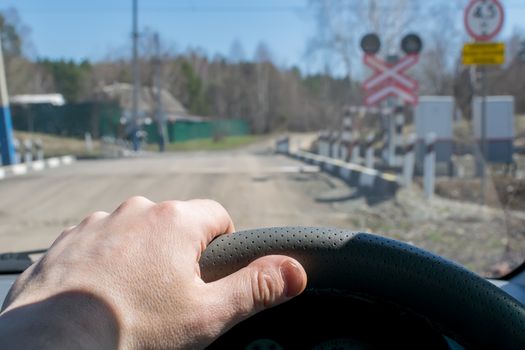 View of the driver's hand on the steering wheel of the car, which stopped before the railway crossing and indicator road signs