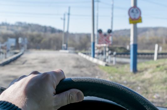 View of the driver's hand on the steering wheel of the car, which stopped before the railway crossing and indicator road signs