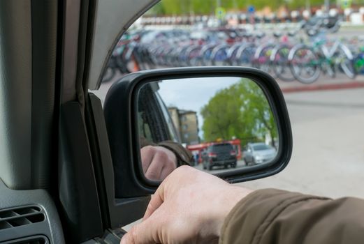 View of the human hand on the open window of the car door, which stands in the Parking lot to the background of selling many new bicycles installed on the street