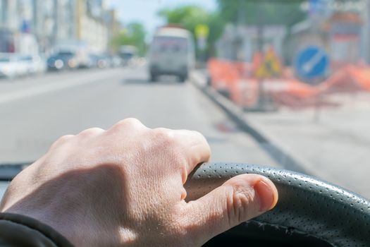 View of the driver's hand on the steering wheel on the background of road repair signs