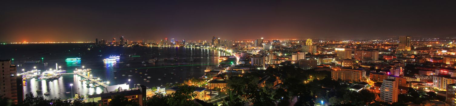 panorama view of pattaya city bay view with building and city night light , boat at dock port. night scene of pattaya city from view point