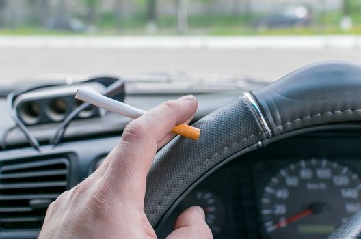 close up, in the hand of the car driver cigarette on the background of the dashboard and the street outside the window