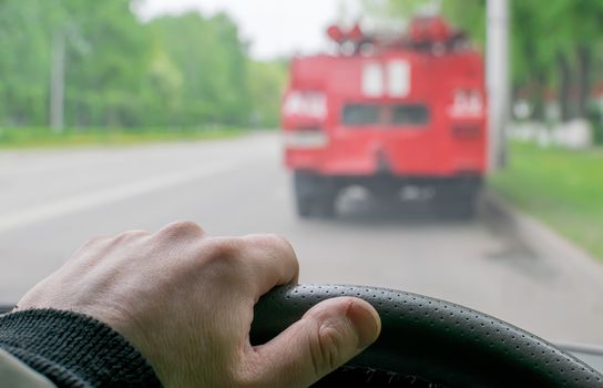 driver hand on the steering wheel of the car on the background of a fire truck on the roadway