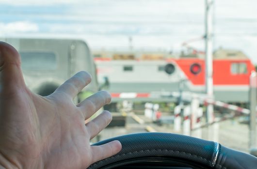 The hand of man inside the car. The car stopped in front of a closed barrier and a red traffic light before the railway crossing. Man outraged by the situation that did not have time to ride the move