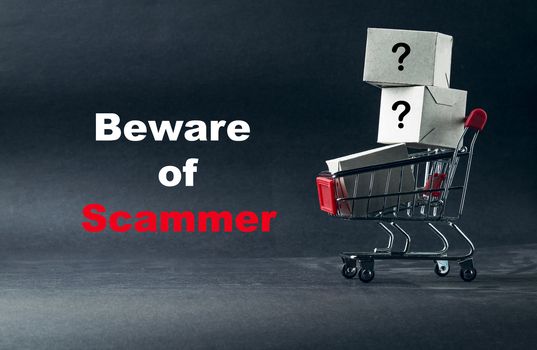 Words BEWARE OF SCAMMER on dark background with shopping cart. Business, Copy space and online shopping concept. Selective focus