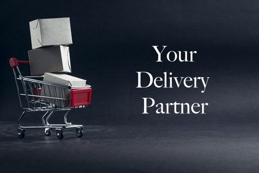 YOUR DELIVERY PARTNER text with shopping cart on dark background. Business, Copy space and online shopping concept. Selective focus