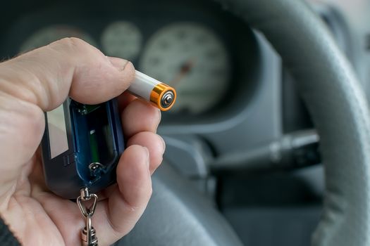 the hand of the person who is in the car holds the disassembled alarm keychain and a new battery for replacement