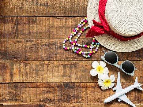 flat lay of hat , necklace , sun glass , flower and red heart shape as traveler's accessories items for summer vacation and plane model on wooden background with copy space. love travel and vacation